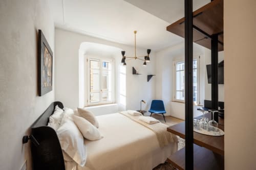 Camera moderna presso Manu Maison a Parma con letto, poltrona blu, lampada a sospensione e ampie finestre luminose