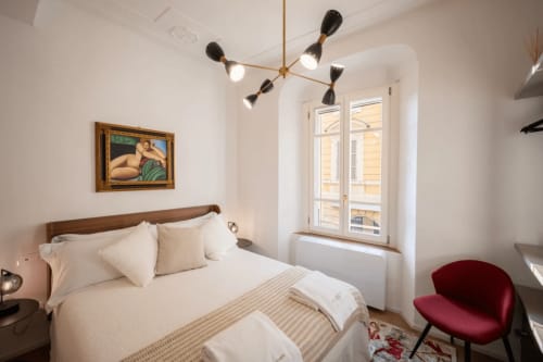 Elegante camera da letto a Manu Maison a Parma con biancheria bianca, letto in legno, lampada a sospensione in ottone e poltrona bordeaux