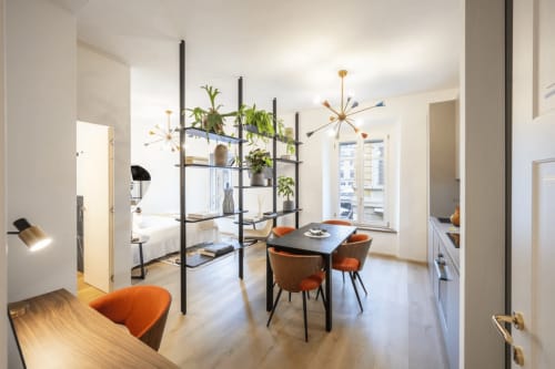 Moderno monolocale a Parma con scaffalature nere, sedie arancioni, tavolo da pranzo e lampade a sospensione mid-century