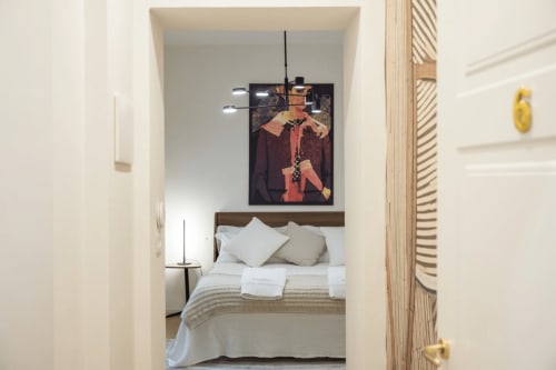Camera moderna al Manu Maison di Parma con letto in legno, biancheria bianca, arte contemporanea e lampade a sospensione.