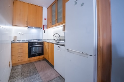 Kompakte Küche mit Holzschränken, weißen Geräten und Granitarbeitsplatten im EcoHost Matosinhos Apartment