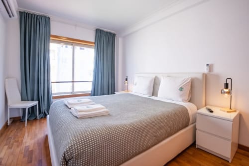 Modernes Schlafzimmer im EcoHost in Matosinhos mit Queensize-Bett, weißem Nachttisch, blauen Vorhängen und Holzfußboden