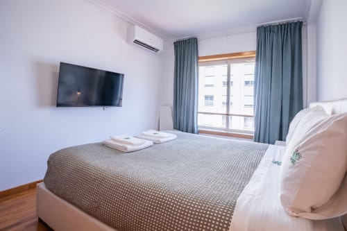 Modernes Schlafzimmer im EcoHost Matosinhos mit Queensize-Bett, Wandfernseher, grauen Vorhängen und Gartenblick