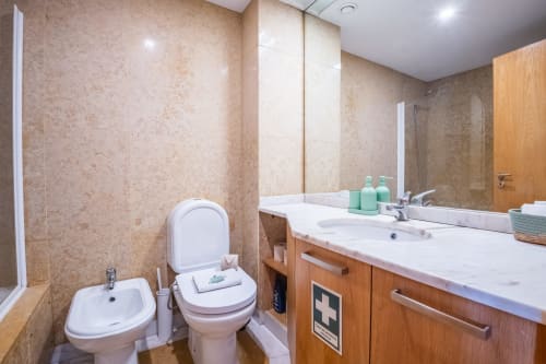 Modernes Badezimmer im EcoHost Apartment in Matosinhos, Portugal, mit Doppelwaschbecken, Toilette, Bidet und beigen Fliesenablaufen