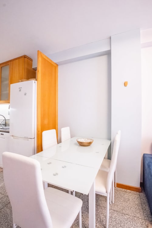 Moderner Essbereich mit weißem Tisch, weißen Stühlen und orangefarbener Holztür in der Küche des EcoHost Matosinhos Apartments