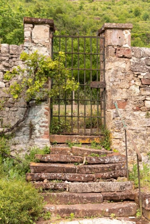 Portail en pierre vieillie avec portail en fer à La Demeure du Comte, Marcillac-Vallon, entouré de verdure luxuriante
