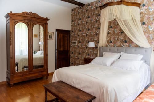Chambre élégante à La Demeure du Comte avec lit à baldaquin, armoire en bois ouvragé, papier peint fleuri et vue sur le jardin