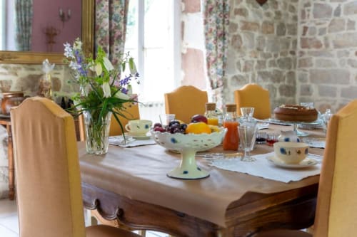 Table de petit-déjeuner élégante à La Demeure du Comte avec chaises jaunes, fleurs fraîches et fruits
