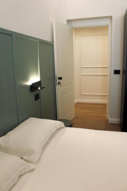 Camera moderna a Maison Riviera a Reggio di Calabria con biancheria bianca, armadio verde e accesso aperto al bagno