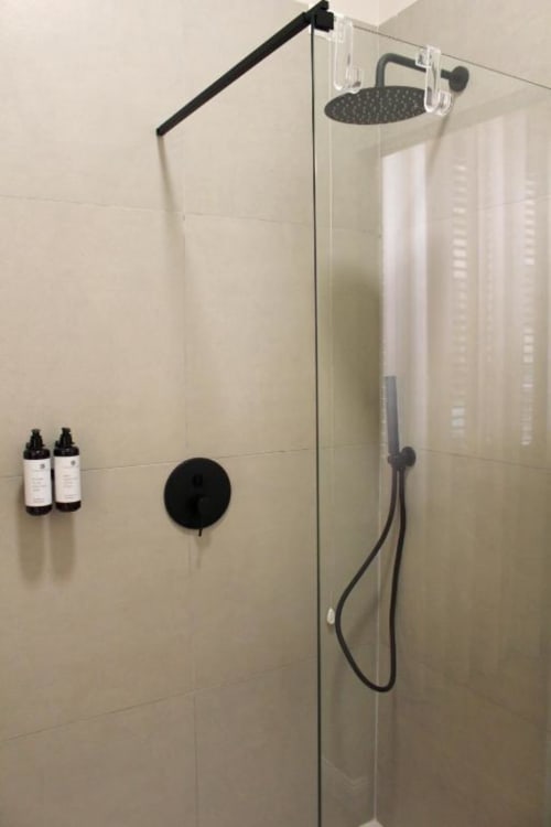 Moderna cabina doccia a Maison Riviera con fixtures neri, soffione a cascata, doccetta manuale e prodotti per il bagno su piastrelle