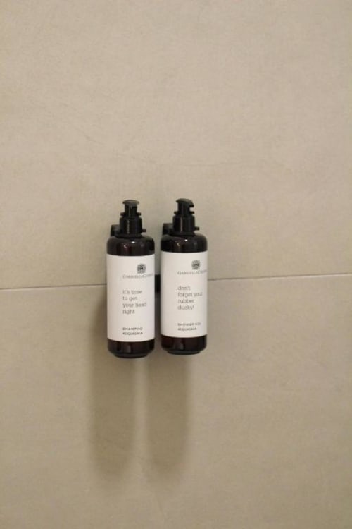 Due bottiglie di vetro scuro con etichette bianche contenenti i prodotti da bagno omaggio dell'hotel boutique Maison Riviera a Reggio di