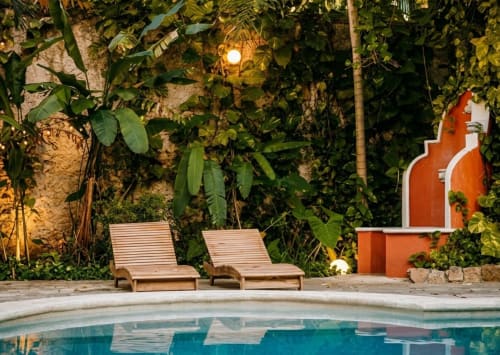 Dos tumbonas de madera junto a la piscina iluminada del Villa Merida Boutique Hotel en Mérida, rodeadas de plantas tropicales
