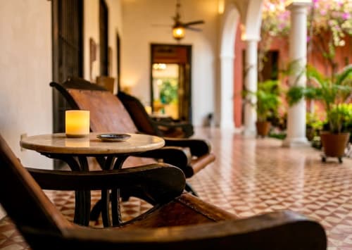 Elegante patio lounge en Villa Merida Boutique Hotel con mesa de madera iluminada por velas, sillas negras y plantas exuberantes.