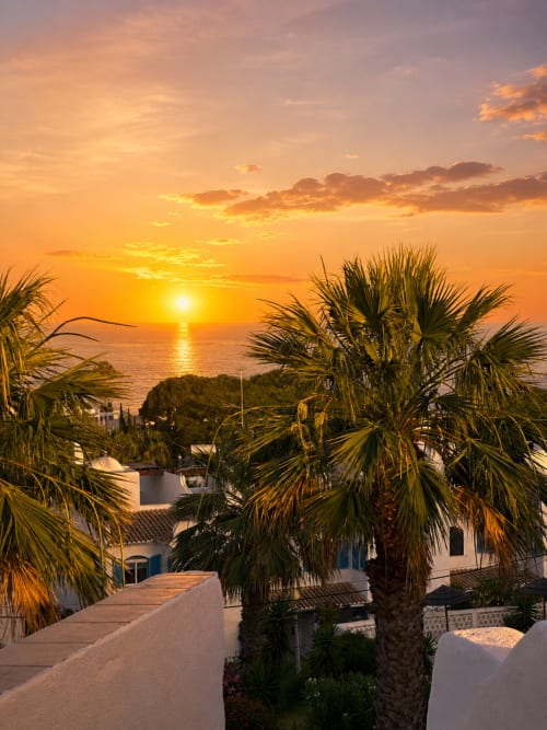 Pôr do sol dourado sobre o Mar Mediterrâneo com palmeiras e edifícios brancos em estilo mediterrâneo do apartamento AlgarStays Algarve