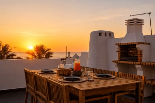 Jantar ao pôr do sol na varanda com vista para o oceano do apartamento AlgarStays Algarve com mesa de madeira, arquitetura branca e vista para o mar