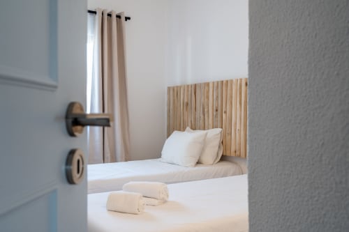 Quarto moderno no apartamento AlgarStays Algarve com cabeceira de madeira, roupa de cama branca e cortinas com vista para o mar