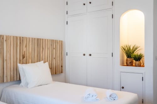 Quarto moderno com cabeceira de madeira, roupa de cama branca e nicho integrado com plantas em vasos no AlgarStays Algarve