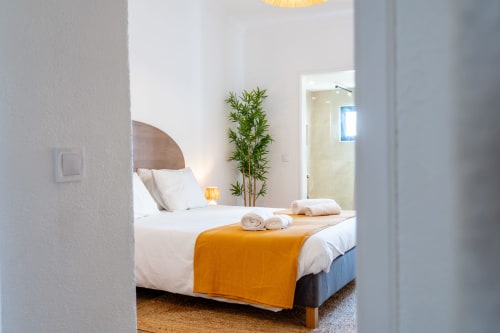 Quarto moderno no apartamento AlgarStays Algarve com vista para o oceano, roupas brancas, manta laranja e planta de bambu