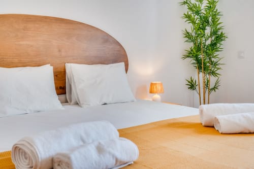 Quarto moderno no apartamento AlgarStays Algarve com cama de madeira, roupas de cama brancas, toalhas enroladas, planta de bambu e iluminação aconchegante