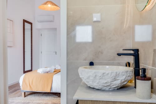 Banheiro moderno com pia de mármore e torneira preta; quarto com manta amarela visível no apartamento AlgarStays no Algarve