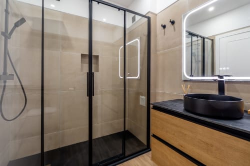 Banheiro moderno com box de vidro com moldura preta, pia oval preta e espelho com iluminação neon no apartamento AlgarStays no Algarve.