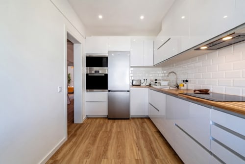 Cozinha branca moderna com bancadas de madeira, eletrodomésticos em aço inoxidável e azulejos tipo metrô na AlgarStays Algarve