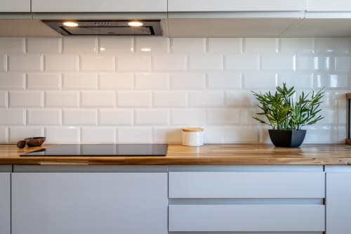 Cozinha moderna com azulejos brancos estilo metrô, bancada de madeira, planta em vaso e eletrodomésticos em aço inoxidável