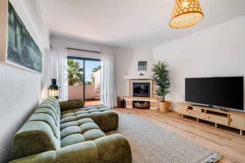 Sala de estar moderna de apartamento com vista para o mar, sofá verde, lareira, TV e acesso ao terraço em AlgarStays Algarve