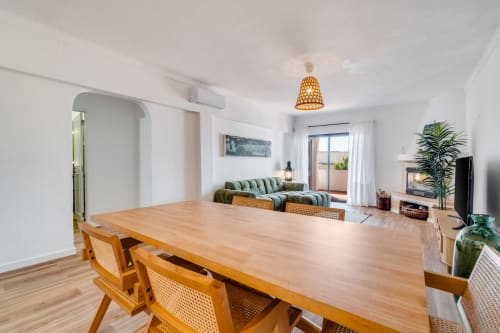 Espaçoso living integrado com sala de jantar bem iluminada, mesa de madeira, cadeiras de vime, sofá verde e vista para o mar em AlgarStays Algarve