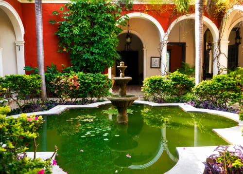 Patio colonial en Villa Merida Boutique Hotel con fuente, columnata arqueada, muros rojo vibrante y exuberante tropical