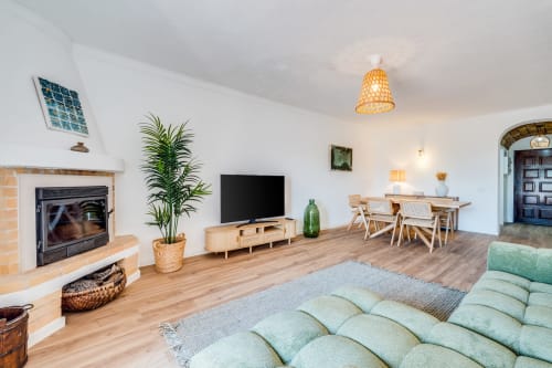Sala de estar moderna no Algarve com lareira, vista para o mar, móveis de madeira, sofá verde e área de refeições