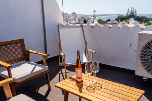 Terraço na cobertura com móveis de madeira, garrafa de vinho e vista para o mar no apartamento AlgarStays Algarve