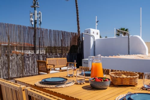 Terraço ensolarado da AlgarStays com mesa de jantar, vista para o oceano, edifício de paredes brancas e cenário costeiro do Algarve