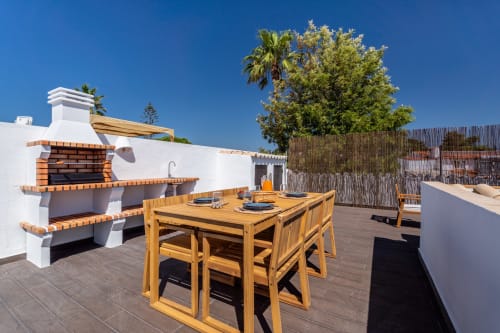Espaçoso terraço na cobertura do apartamento AlgarStays Algarve com mesa de jantar em madeira, churrasqueira de tijolos e vista para o mar