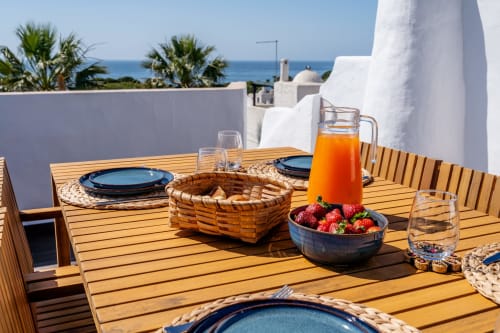 Terraço à beira-mar do apartamento AlgarStays Algarve com louça azul, morangos frescos, suco de laranja e vista para o mar