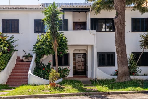 Edifício mediterrâneo branco em Alporchinhos, Algarve com palmeiras, escadas de tijolos vermelhos e acesso com vista para o mar