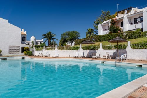 Piscina de luxo no resort AlgarStays Algarve com apartamentos brancos, espreguiçadeiras, guarda-sóis e vista para o mar