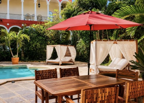 Área lounge de lujo junto a la piscina en Villa Merida Boutique Hotel con mesa de comedor de madera, sombrilla roja y camas cabana en Mérida