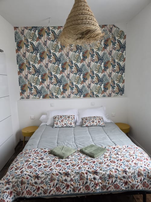 Cottage bedroom at STE CATALAUNES with botanical patterned headboard, white bedding, and woven hanging lamp accent.