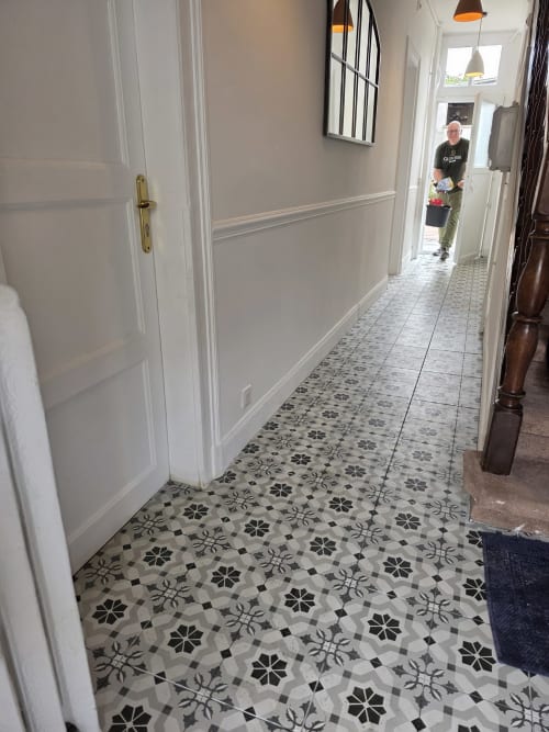 Modern hallway with geometric patterned tile flooring, white paneled walls, and pendant lighting in Gîte de la cité Tirlet