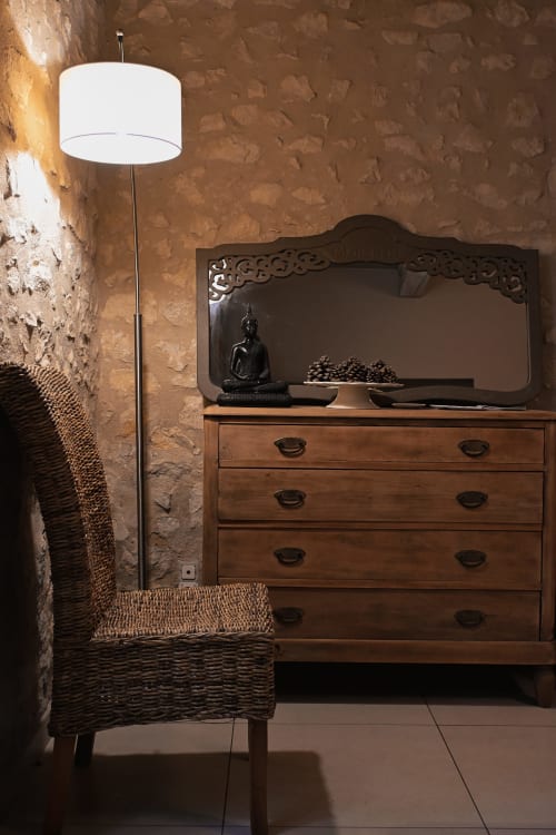 Coin chambre douillet au Mas De La Digue avec fauteuil tressé, commode bois, miroir, statuette Bouddha et lampadaire moderne