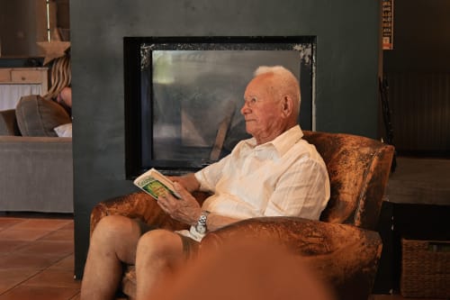 Un homme senior lisant dans un fauteuil en velours marron à Mas De La Digue, gîte à Châteaurenard, France