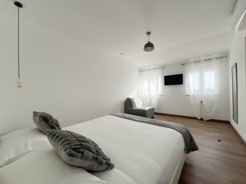 Quarto moderno do hotel Monte Horeb em Nadadouro com cama branca, TV, janelas com vista para a piscina e iluminação contemporânea