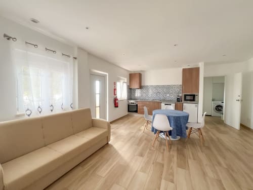 Apartamento de planta aberta moderno no Alojamento Local Monte Horeb com sofá bege, cozinha equipada, sala de refeições e acabamentos em madeira