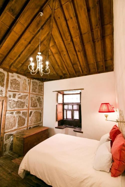 Dormitorio rústico con techo de madera, cama blanca, cojines rojos y pared de piedra en Casa 1820, La Palma