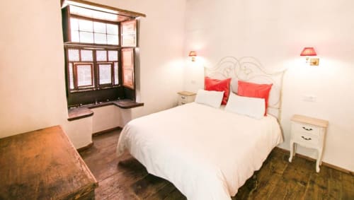 Dormitorio con cama blanca, almohadas rojas, ventana de madera, mesitas de noche e iluminación cálida en Casa 1820, apartamento rural en Santa