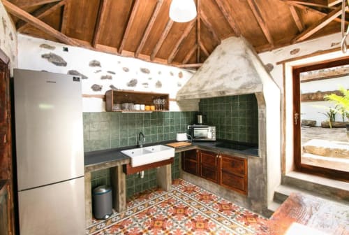 Cocina Casa 1820 con vigas de madera expuestas, azulejos verdes, fregadero blanco y piso con patrón decorativo en Santa Cruz