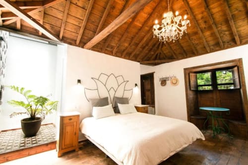 Dormitorio espacioso en Casa 1820, Santa Cruz de la Palma, con cama blanca, vigas de madera, araña y vistas al jardín