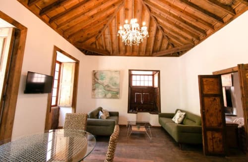 Amplia sala de estar en Casa 1820 con vigas de madera vista, araña, sofás verdes, TV y puertas de madera hacia el jardín