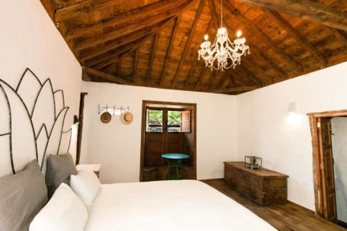Dormitorio rústico en Casa 1820, Santa Cruz de la Palma, con vigas de madera, cama blanca, lámpara de araña y vistas al jardín